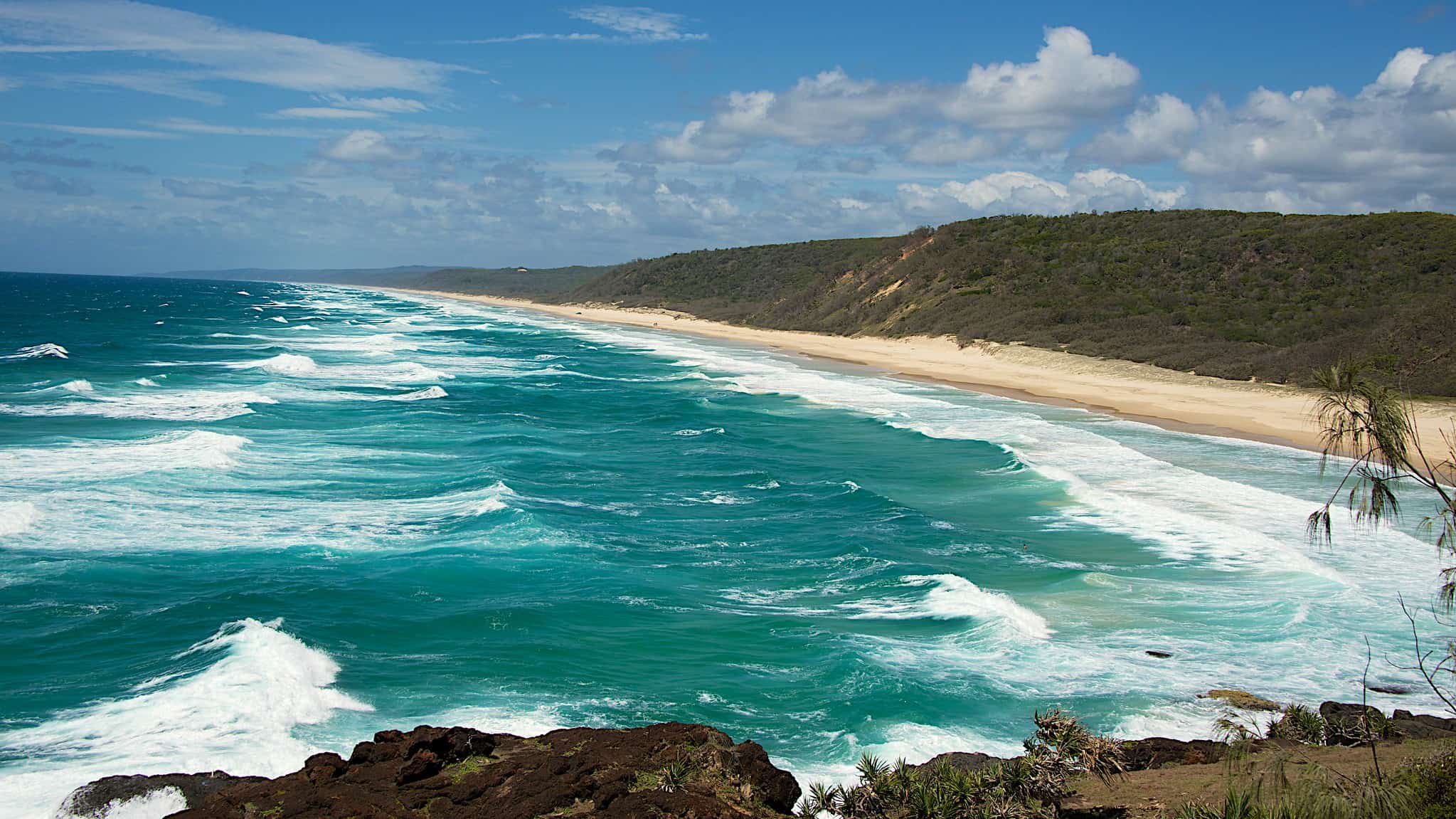 View of Rainbow Beach with the sea on the left with waves crashing and the ling sand beach on the right