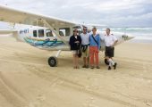 People standing in front of a plane on the beach